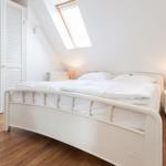 Schlafzimmer mit Dachschräge, weißem Bett und Holzboden