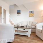 Wohnzimmer mit Sofa, zwei Sesseln und Holzboden. An der Wand hängen zwei Bilder.