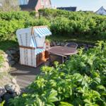 Gartenbereich mit Strandkorb, Tisch und Stühlen. Umgeben von Grünflächen und Steinmauern.