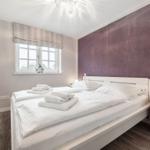 Bedroom with white bed, purple wall, and wooden side table.