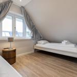 Room with two beds, wooden floor, and large window with curtains.