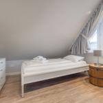 Bedroom with bed, TV, and window. Wooden floor and wooden barrel nightstand.