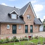 A two-story house with brick facade and gray roof. Front garden with flowers and bike rack.