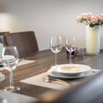 Set dining table with glasses, plates, and flowers in the background.