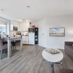 Living kitchen with dining table, sofa, and TV. Wooden floor and white kitchen area.