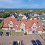 Large house with red roof and solar panels, view of beach and dunes.