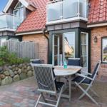 Terrace with table and chairs in front of a brick house with red roof.
