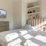 Bedroom with double bed, dresser, and wall picture. Shelf with decorative items.