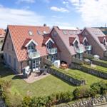 Holiday home with red roof and balconies, surrounded by lawns and stone walls.