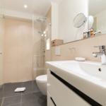 Bathroom with shower, sink, and toilet. Mirror, towel, and tiles visible.