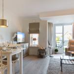 Dining area with table and chairs, living area with sofa and armchair, window to terrace.