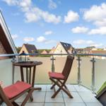 Balcony with two wooden chairs and a table. View of houses and sky.