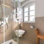 Bad mit Dusche, Toilette und Holzbank. Fenster mit Pflanze.