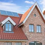 Rotes Ziegeldach mit Solaranlage und Dachfenster an einem Backsteinhaus.