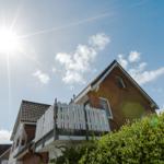 House with balcony under bright sunlight and blue sky with white clouds.