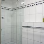 Shower cabin with glass door and white tiles. Two green bottles on the wall.