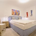 Schlafzimmer mit Bett, Nachttisch und Stühlen. Wandbild und Fenster sichtbar.