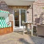 Terrasse mit Strandkorb, Tisch und Stühlen vor einer Glasfront.