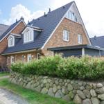 House with brick facade, dark roof, and stone wall with berry bushes.