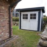 Behind the house is a small shed with white doors and dark siding.