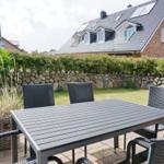 Terrace with table and chairs, lawn and stone wall in background.