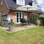 Backyard with terrace, parasol, and garden furniture. Lawn and plants surround the terrace.