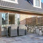 Terrasse mit Tisch und Stühlen vor einem Haus mit Steinmauer und Holzzaun.