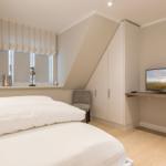 Schlafzimmer mit Dachschräge, Bett, Schrank und TV.