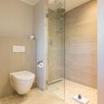Dusche mit Glaswand, Toilette und Handtuch auf Steinboden.
