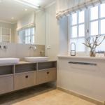 Badezimmer mit zwei Waschbecken, Spiegelschrank und Fenster mit Vorhang.