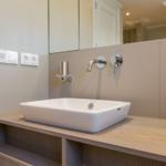 Waschbecken mit Spiegel und Wasserhähnen auf Holzkonsole