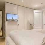 Schlafzimmer mit weißem Bett, Kleiderschrank und Fernseher an der Wand.