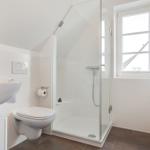 Bathroom with shower, toilet, and sink. Window and towel rack visible.
