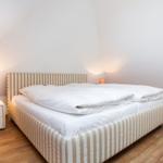 Bedroom with bed, nightstand, and lamp. Wooden floor and sloped ceiling.