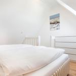 Bedroom with white bed, wooden floor, and sloped ceiling.