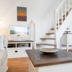 Living room with TV, sofa, and storage unit. Wooden staircase leads to upper level.
