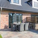 Terrace with table and chairs in front of a brick house with dormers.