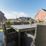 Terrace with table and chairs, view of houses and green areas.