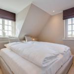 Bedroom with double bed, two windows, and wooden floor.