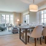 Dining room with table and chairs. Living area with armchair and windows.