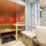 Sauna with wooden bench and red light, beside freestanding tub and window.
