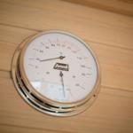 Wall thermometer in sauna shows temperature and humidity.