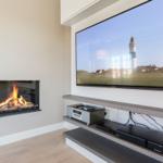 Fireplace with burning logs and wall-mounted TV showing a lighthouse.