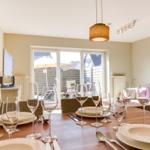 Set dining table with glasses and plates. Large window opens to garden.