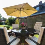 Terrace with seating, sunshade, and flowers. Background: garden and house.