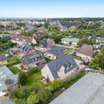 Aerial view of a residential area with houses, gardens, and a view of the sea.