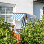 Blue-and-white beach chair between green shrubs in front of white house