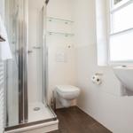 Bathroom with shower, toilet, and sink. Window with blinds.