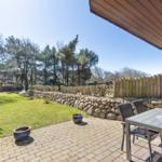 Terrace with table and chairs, paved ground, lawn, and stone wall in background.