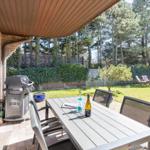 Terrace with table, chairs, and grill. Backyard with lawn and trees.